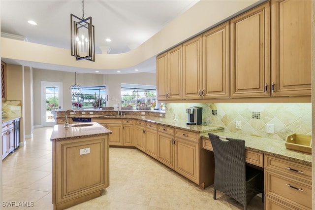 kitchen featuring pendant lighting, sink, light stone counters, and a kitchen island with sink