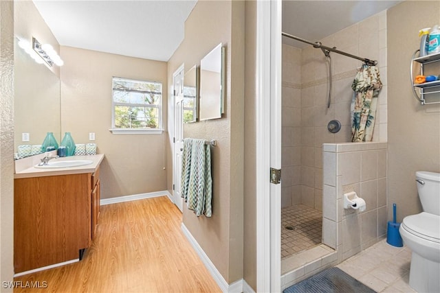 full bath featuring toilet, wood finished floors, a tile shower, baseboards, and vanity