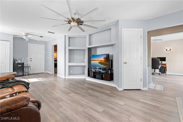 living area with visible vents, built in shelves, a ceiling fan, light wood-style floors, and baseboards