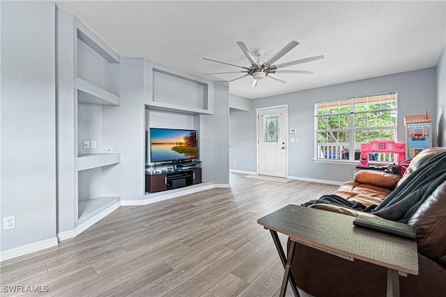 living room with built in features, baseboards, wood finished floors, and a ceiling fan