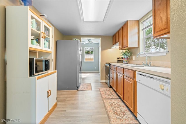 kitchen featuring light wood finished floors, under cabinet range hood, light countertops, appliances with stainless steel finishes, and a sink