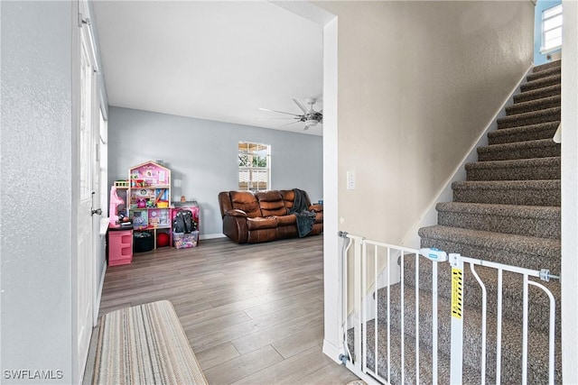 stairway with baseboards, wood finished floors, and a ceiling fan