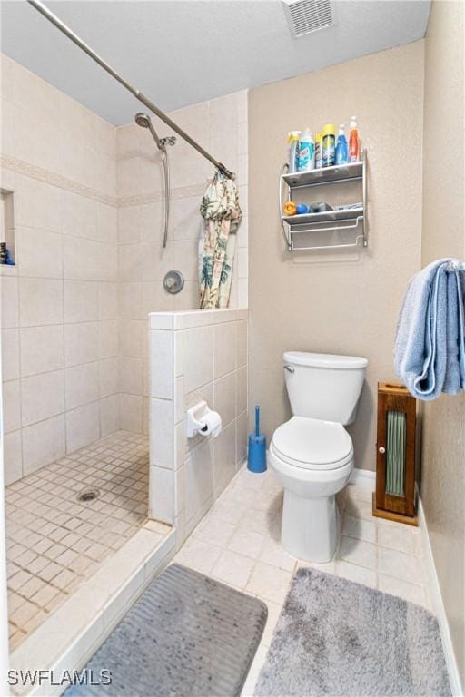 bathroom featuring visible vents, toilet, baseboards, tile patterned flooring, and tiled shower