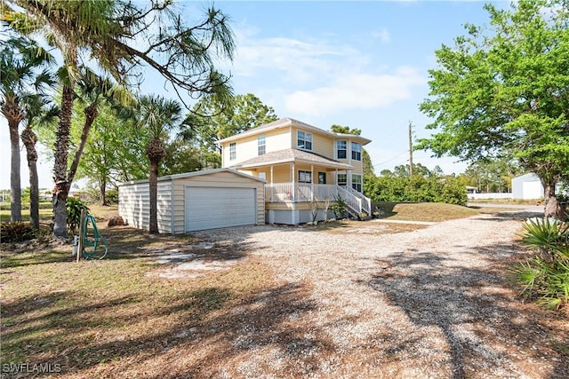 rear view of property with a detached garage, an outdoor structure, covered porch, and driveway