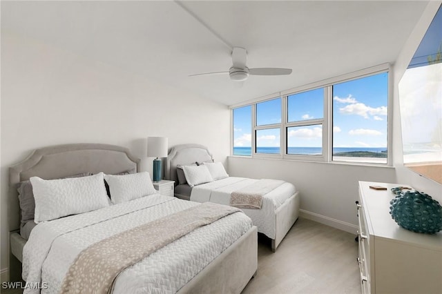 bedroom with light wood-type flooring, ceiling fan, and a water view