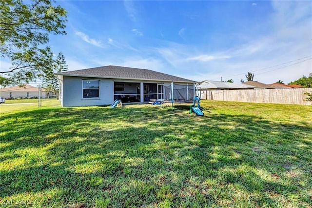 rear view of property with a trampoline and a lawn