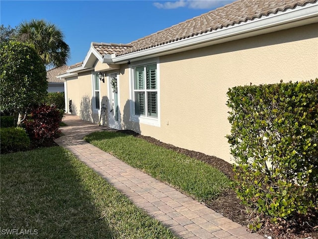 view of side of property with a tiled roof, a lawn, and stucco siding