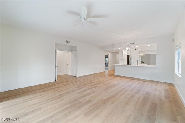 unfurnished living room featuring ceiling fan with notable chandelier and light hardwood / wood-style flooring