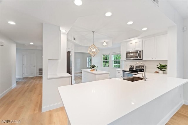 kitchen featuring light hardwood / wood-style flooring, kitchen peninsula, pendant lighting, stainless steel appliances, and white cabinets