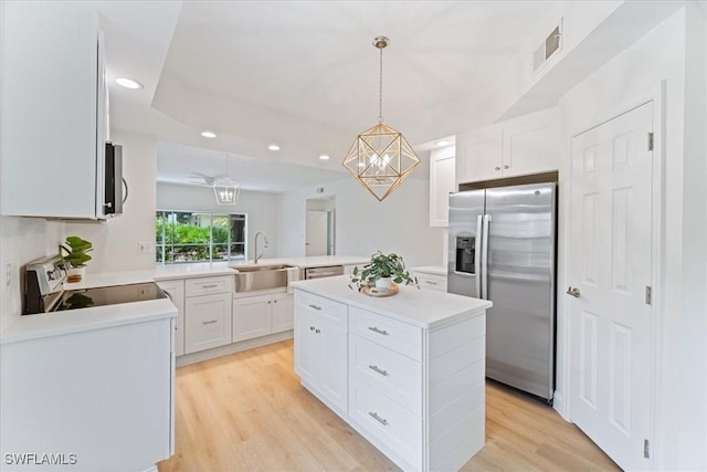 kitchen featuring decorative light fixtures, white cabinets, stainless steel fridge, a center island, and range