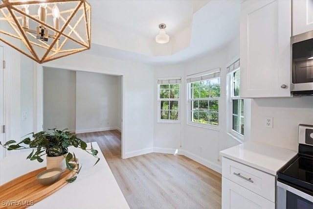 kitchen featuring appliances with stainless steel finishes, a tray ceiling, light hardwood / wood-style flooring, and white cabinets