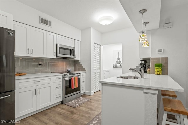 kitchen featuring appliances with stainless steel finishes, decorative light fixtures, sink, and white cabinets