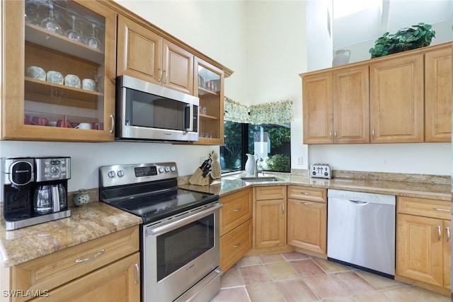 kitchen with stainless steel appliances, light stone countertops, and sink