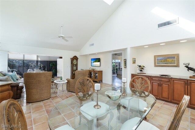 tiled dining space with ceiling fan, a skylight, and high vaulted ceiling