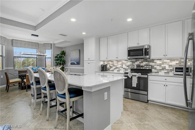 kitchen featuring tasteful backsplash, white cabinets, an island with sink, stainless steel appliances, and a sink