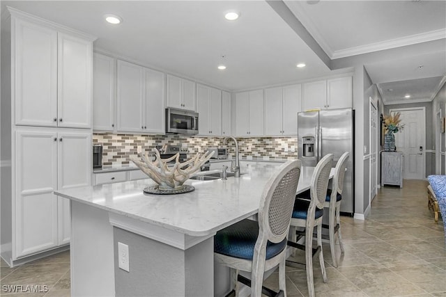 kitchen with white cabinets, appliances with stainless steel finishes, ornamental molding, a kitchen island with sink, and a sink