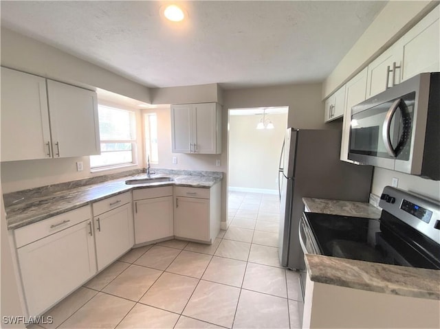 kitchen featuring white cabinets, appliances with stainless steel finishes, an inviting chandelier, a sink, and light tile patterned flooring