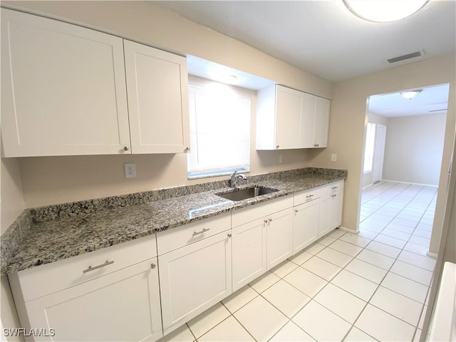 kitchen with visible vents, white cabinetry, a sink, light tile patterned flooring, and dark stone countertops