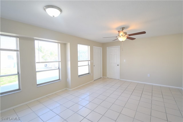 empty room featuring light tile patterned floors, plenty of natural light, a ceiling fan, and baseboards