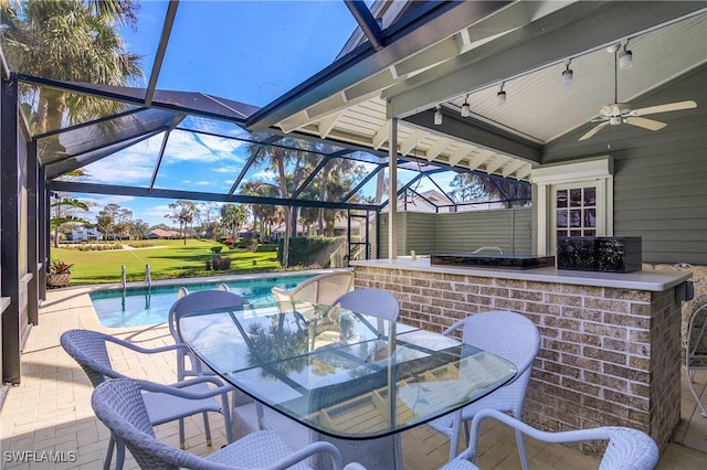 view of patio featuring ceiling fan, glass enclosure, and a bar