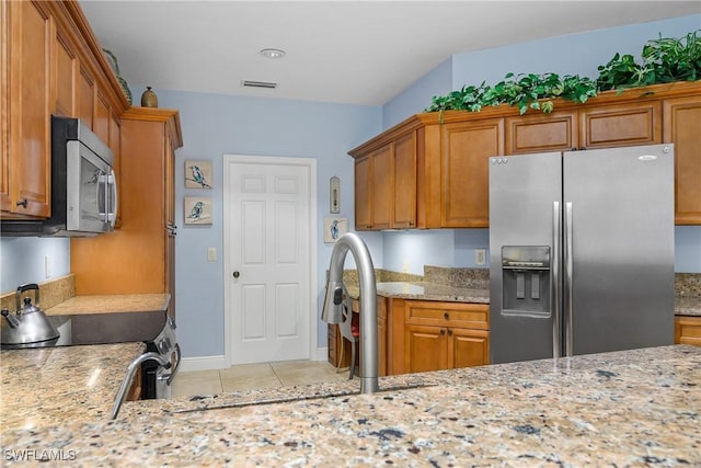 kitchen featuring stainless steel appliances, light tile patterned flooring, and light stone countertops