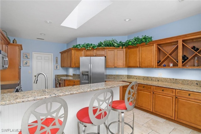 kitchen with stainless steel appliances, light stone countertops, a breakfast bar, and a skylight