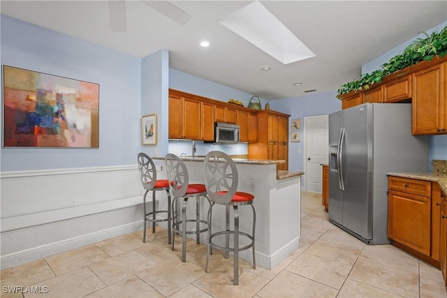 kitchen with a breakfast bar area, light stone counters, a skylight, light tile patterned floors, and appliances with stainless steel finishes