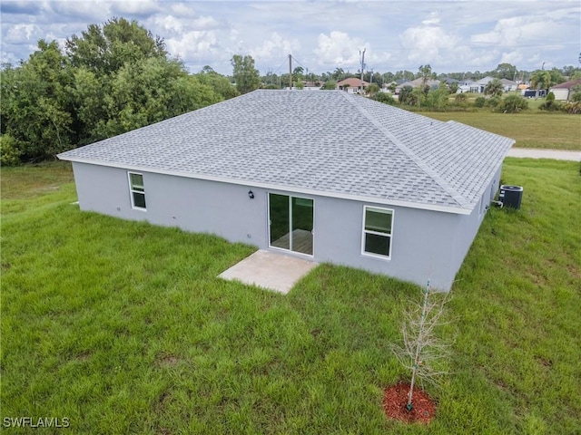 rear view of property with a shingled roof, central AC unit, a patio, and a yard