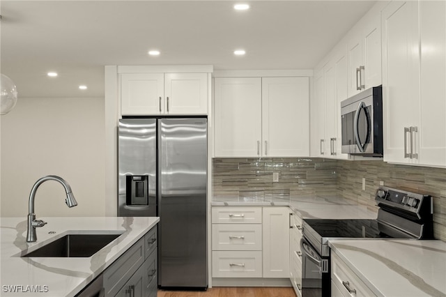 kitchen with stainless steel appliances, white cabinetry, a sink, and light stone counters