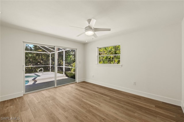 empty room featuring a ceiling fan, wood finished floors, a sunroom, and baseboards