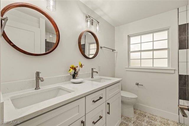 bathroom with baseboards, a sink, toilet, and double vanity