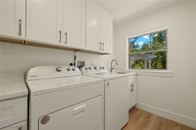 clothes washing area featuring separate washer and dryer, a sink, baseboards, cabinet space, and light wood finished floors