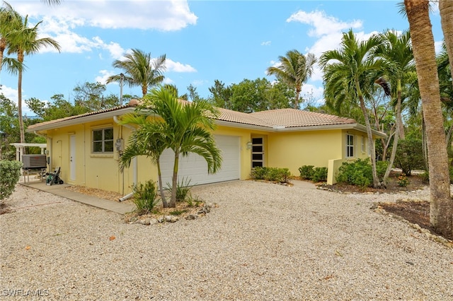 exterior space with an attached garage, cooling unit, a tile roof, stucco siding, and gravel driveway