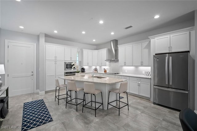 kitchen with a kitchen island with sink, wall chimney exhaust hood, appliances with stainless steel finishes, and white cabinetry