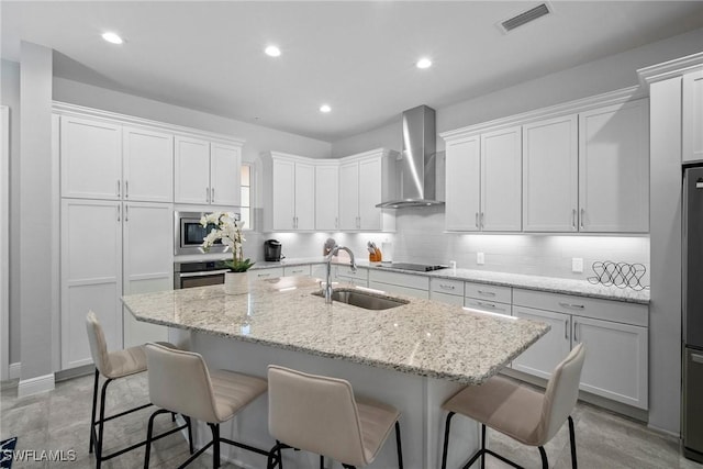 kitchen featuring a kitchen island with sink, a sink, visible vents, and wall chimney exhaust hood