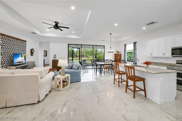 living room featuring ceiling fan with notable chandelier, a raised ceiling, and sink