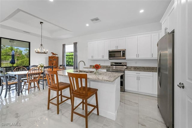 kitchen with sink, appliances with stainless steel finishes, white cabinetry, hanging light fixtures, and an island with sink