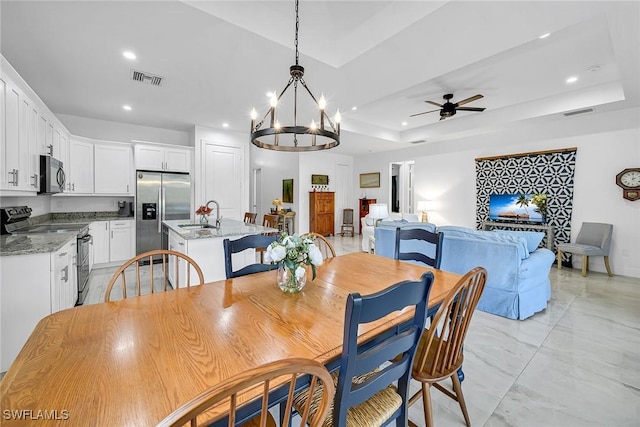 dining space with sink, a tray ceiling, and ceiling fan with notable chandelier