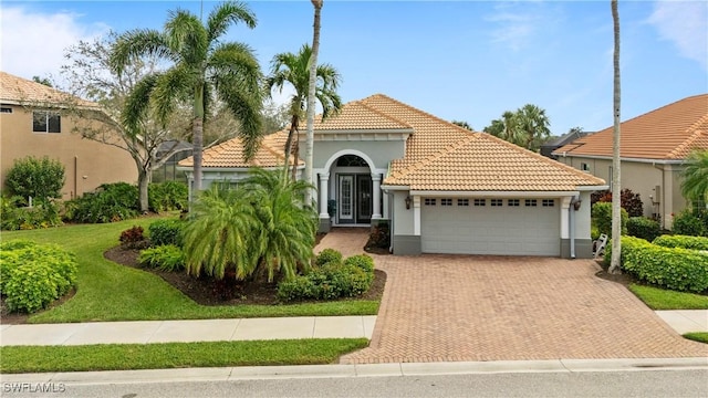 mediterranean / spanish house with a garage, decorative driveway, a tile roof, and stucco siding