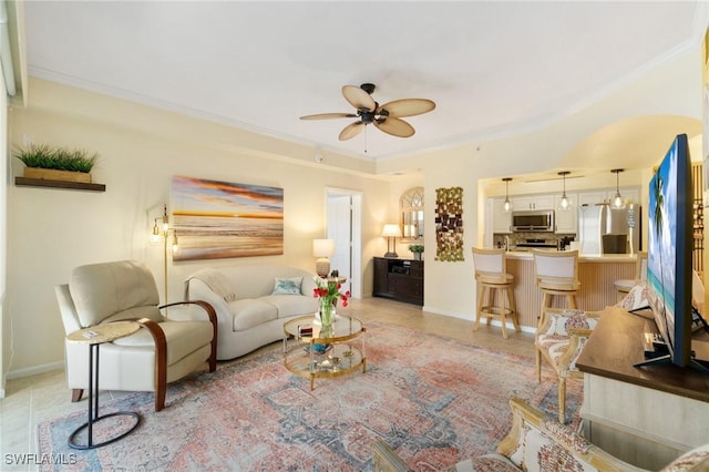 living area with light tile patterned floors, ceiling fan, ornamental molding, and baseboards