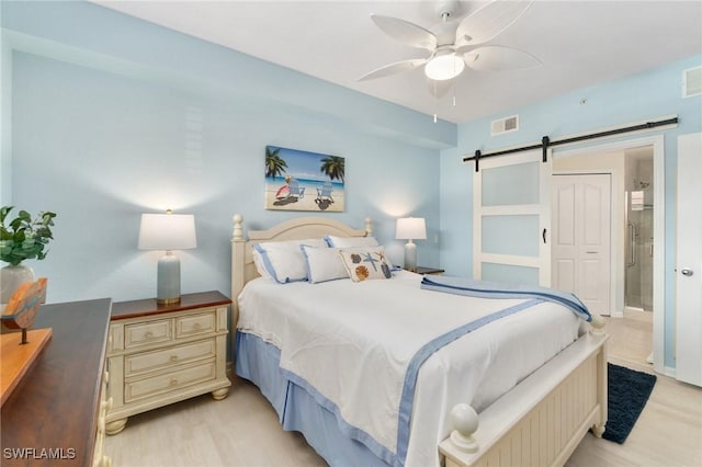 bedroom featuring visible vents, light wood finished floors, and a barn door