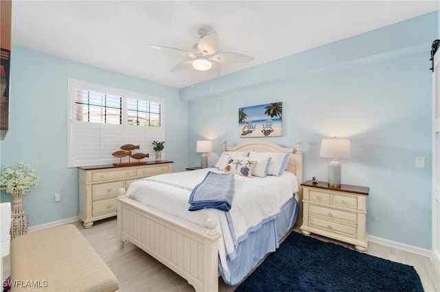 bedroom with a ceiling fan, light wood-style flooring, baseboards, and a barn door