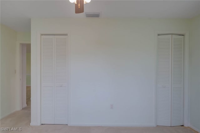 unfurnished bedroom with light colored carpet, two closets, and visible vents