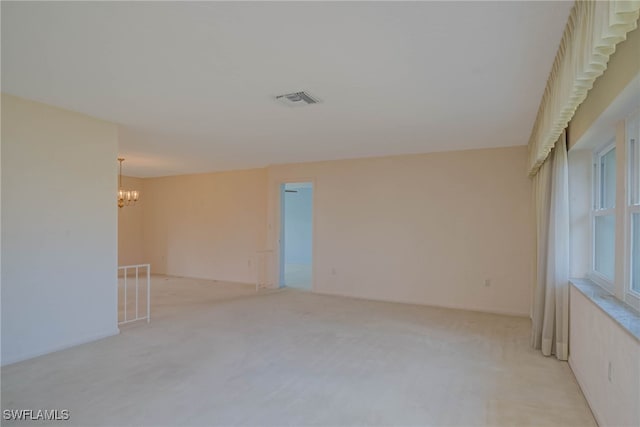 empty room with visible vents, light carpet, and a chandelier