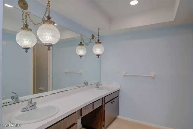 full bathroom featuring a sink, baseboards, a tray ceiling, and double vanity