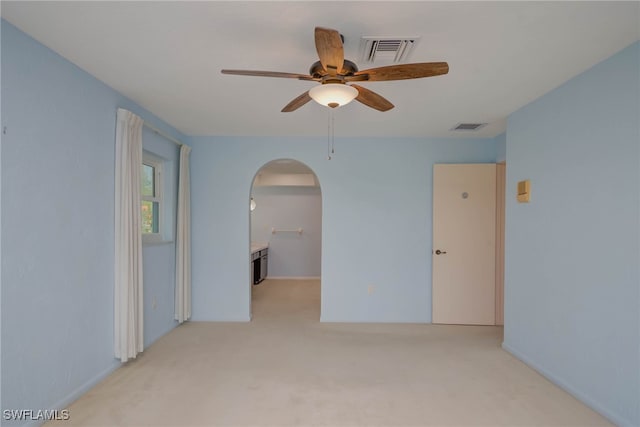 unfurnished room with light colored carpet, a ceiling fan, visible vents, and arched walkways