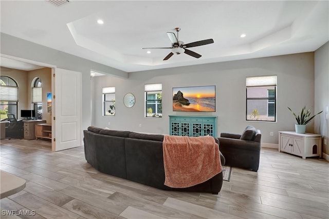 living room with baseboards, a raised ceiling, a ceiling fan, light wood-style flooring, and recessed lighting