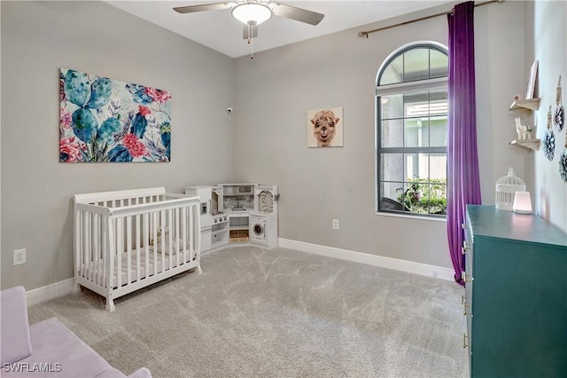 carpeted bedroom with a nursery area, ceiling fan, and baseboards