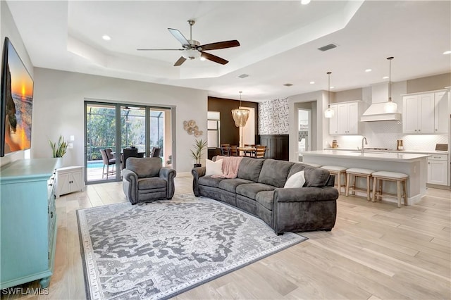 living area with ceiling fan, recessed lighting, visible vents, light wood-type flooring, and a tray ceiling