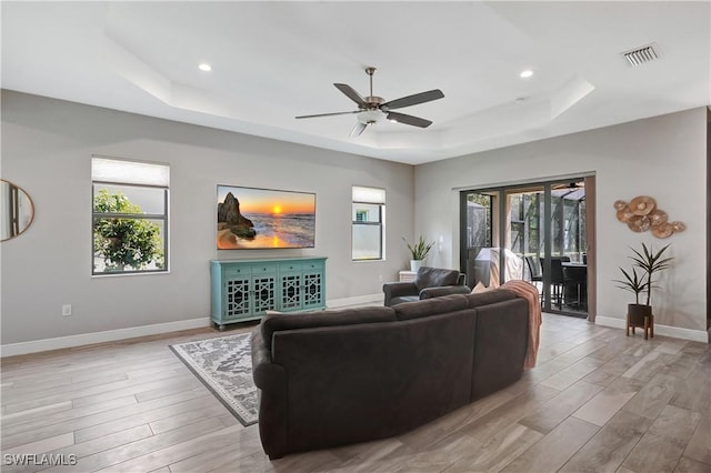 living room with a healthy amount of sunlight, light wood-style flooring, visible vents, and a raised ceiling